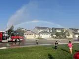 Firefighter on back of Fire Engine spraying water in the air getting kids wet in a neighborhood